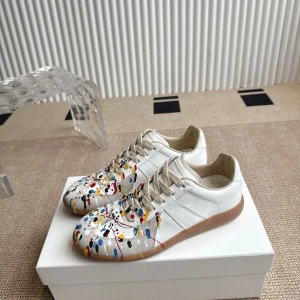 Gats paint splatter - Maison margiela vita sneakers med coola färgstänk i blått, rött, gult och svart över tån och sidorna. Skorna har beige snörning, vit ovandel i skinn och en klassisk gummisula i brunt. Perfekt för dig som vill sticka ut med en kreativ och konstnärlig vibe.