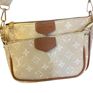 Beige axelväska  - Snygg beige axelväska . Väskan har två fack med dragkedja, bruna skinn-detaljer och bred axelrem med logga. Perfekt för dig som vill ha en trendig och praktisk väska med lyxig känsla.