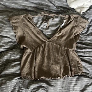 Brun topp - Supersöt beige blus från 157 med v-ringning och volangärmar. Toppen har knyt i ryggen och lätt rynkad nederkant för en avslappnad look. Tillverkad i ett mjukt, tunt tyg som känns luftigt och skönt. Perfekt för dig som gillar en feminin och chill stil. Köpt sexond han men i fint skick🩷