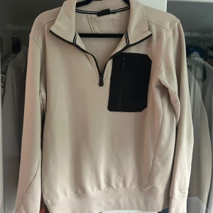 Beige Sail Racing half zip tröja S - Snygg beige långärmad tröja från Sail Racing i storlek S. Tröjan har svart bröstficka med dragkedja och halv dragkedja framtill. Perfekt för lager-på-lager och har en clean look med sportig känsla. Passar dig som gillar stilrena och funktionella plagg.