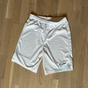 Vita Nike Dri-Fit shorts (XL barn) 158-170 cm - Snygga vita träningsshorts från Nike i Dri-Fit-material. Klassisk passform, perfekt för sport eller chill. Nike-logga i svart på ena benet. Lätta och luftiga.