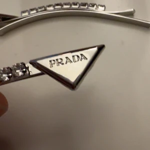 silverfärgade hårspännen med stenar - Snygga hårspännen  silverfärg med glittrande stenar längs hela bågen. Triangelformad detalj med ingraverad P-logga ger en lyxig och trendig känsla. Perfekta för dig som vill sticka ut med exklusiva accessoarer.