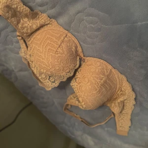Beige spets-bh från Intimissimi 75D - Säljer en superfin beige bh från Intimissimi i storlek 75D. HELT NY. Bh:n är täckt av vacker spets med blommigt mönster och har en liten rosett mellan kuporna. Perfekt för dig som gillar romantiska detaljer och snygg passform.