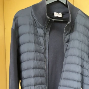 Svart Cardigan jacka från Moncler - Säljer en svart dunväst från Moncler med quiltad design och dragkedja framtill. Västen har en stilren look med diskret logga på ärmen och är tillverkad i polyester. Perfekt för lager-på-lager och snygg till både hoodie och t-shirt.