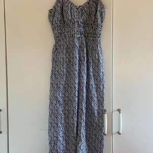 Blåvit långklänning från H&M XS - Snygg långklänning från H&M i storlek XS med blått och vitt grafiskt mönster. Klänningen har resår i midjan och är ärmlös, perfekt för varma dagar. Tillverkad i mjuk bomull som känns skön mot huden.