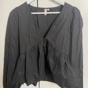 Svart blus med v-ringning och knappar - Supersöt svart blus med långa ärmar, volangdetaljer och en lös passform. Aldrig använd. Kontakta vid frågor osv 😊