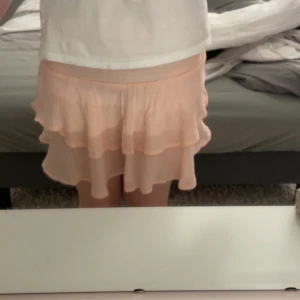 Ljusrosa volangkjol med resår - Supersöt ljusrosa kortkjol med dubbla volanger och bred resår i midjan. Kjolen är luftig och flowy, perfekt för varma dagar. Den har en feminin och lekfull vibe som passar till många olika stilar.