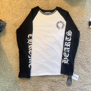 Chrome hearts longsleeve  - Säljer en långärmad tröja från Chrome Hearts med svartvita kontraster. Tröjan har svarta ärmar med stora vita tryck och vit framsida med Chrome Hearts-logga på bröstet och stort tryck på ryggen. Crewneck med tryckt text i halsen. Perfekt för dig som gillar streetwear.