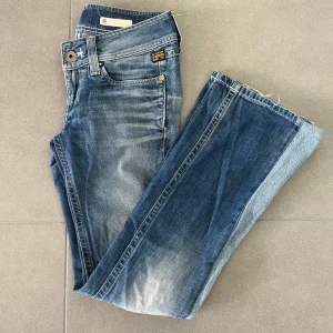 G-Star RAW blå bootcut jeans - Snygga blå jeans från G-Star RAW med bootcut passform och låg midja. Jeansen har slitningar och tvärfeta detaljer som tvätten och den markerade sömmen vid benet!! Storlek W26 och L32!! Är öppen till prisförslag.🌟😚 Kolla efter fler snygga jeans i min profil!!