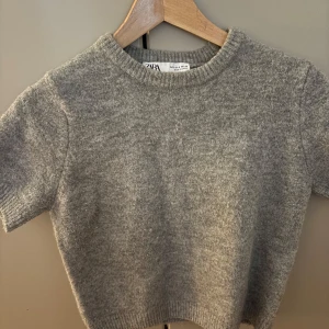 Grå stickad tröja från Zara - Mysig grå stickad tröja från Zara med korta ärmar. Super fin och väldigt trendig. Även i bra skick och knappt använd.