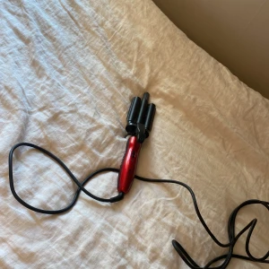 Röd vågtång för håret - En snygg vågtång med röd handtag och svarta värmeplattor, perfekt för att skapa beach waves eller volym i håret. Utrustad med sladd och enkel on/off-knapp. Passar dig som vill fixa frisyren snabbt och enkelt hemma.
