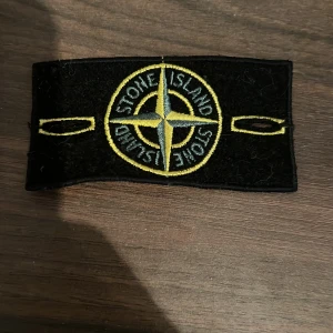 Svart broderad patch från Stone Island - Svart patch med broderad kompasslogga i gult och grått från Stone Island. Perfekt för att fästa på jackor eller tröjor för en stilren look.