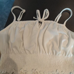 Vit linnetopp från Trendyol i storlek M - Säljer en söt vit linnetopp från Trendyol med smala axelband och knytning framtill. Toppen har en elastisk smockdetalj vid midjan som ger en fin passform. Perfekt för varma sommardagar! 🌞