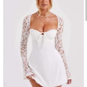 Vit spetsklänning med långa ärmar - Säljer en elegant vit klänning med spetsdetaljer och långa ärmar. Klänningen har en söt knytning framtill och en figurnära passform. Perfekt för speciella tillfällen.