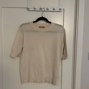 Cremevit tröja  - Säljer en stilren cremevit tröja från Åhléns med rund hals och trekvartsärmar. Perfekt för en minimalistisk look. Tröjan har ribbade kanter vid ärmslut och nederkant.