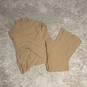 Beige tröja och utsvängda byxor matchande set  - Säljer en stilren beige ribbad polotröja med långa ärmar och matchande utsvängda byxor. Perfekt för en avslappnad och trendig look. Tyget är mjukt och setet är från bikbok