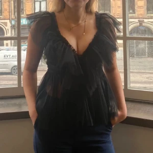 Svart volangblus - Säljer en elegant svart blus med volangdetaljer. Blusen är ärmlös och har en v-ringad design som ger en stilren look. 💘