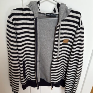 Randig hoodie från Dolce & Gabbana - Säljer en snygg randig hoodie från Dolce & Gabbana i svart och vit. Tröjan har en dragkedja framtill och en bekväm huva i grått. Storlek 50 eventuellt M