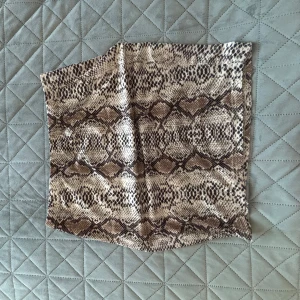 Kjol med ormmönster - Snygg kjol med ett coolt ormmönster i bruna och beige toner. Perfekt för att ge din outfit en edgy touch. Materialet är mjukt och bekvämt att bära. Passar bra till både jackor och tröjor.