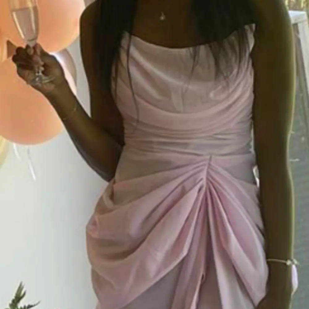 Elegant ljusrosa klänning med draperad design och hög slits. Axelbandslös stil som ger en sofistikerad look. Perfekt för speciella tillfällen.. Mekot.