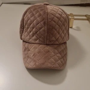 Beige quiltad keps - Snygg beige keps med quiltat mönster. Perfekt för en stilren look. Kepsen har en klassisk design med böjd skärm och justerbar passform.