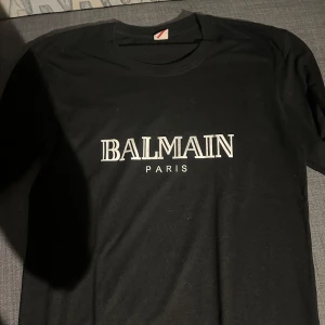 Svart t-shirt från Balmain - Snygg svart t-shirt från Balmain med vit logga på bröstet. Perfekt för en stilren look. Passar till både jeans och kjol. 🖤