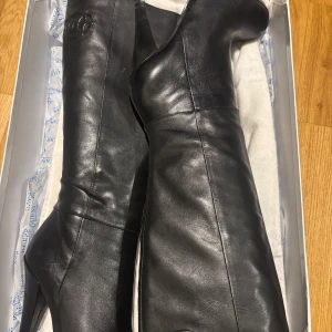 Svarta stövlar med klack och dragkedja - Snygga svarta stövlar från Guess i skinn med hög klack och dragkedja på sidan. Perfekta för en stilren look. Sulan har ett mönster med Guess-logotypen, priser klan förhandlas