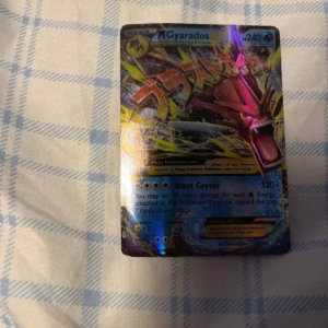 Pokémonkort Mega Gyarados - Säljer ett Pokémonkort med Mega Gyarados. Kortet har en färgglad och glansig design med Gyarados i en kraftfull pose. Det är en del av Pokémon Trading Card Game och har en hög attackstyrka. Perfekt för samlare eller spelare som vill förstärka sin kortlek.