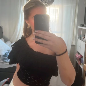 Svart offshoulder topp med volang - Snygg svart offshoulder topp med volangdetaljer. Perfekt för en kväll ute eller en speciell tillställning. Toppen har en elegant och trendig design som framhäver axlarna.