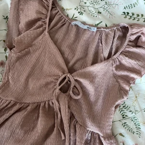 Rosa blus med knytning - Säljer en söt rosa blus med volangdetaljer och knytning framtill. Blusen har en luftig passform och korta ärmar, perfekt för varmare dagar. Passar både till jeans och kjol för en avslappnad look. 💕🫶