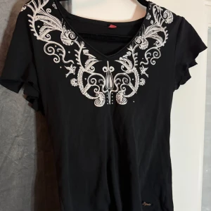 Svart t-shirt med vita detaljer  - !LÄS BIO INNAN KÖP! Svart V-ringad t-shirt med med vita detaljer runt halsringningen. T-shirten har korta ärmar och har ”cuts” (se bild 2) vid axlarna som tillhör designen. Om fler bilder önskas hör av er!