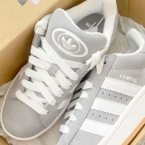 Grå Adidas Campus sneakers - Säljer ett par stilrena grå Adidas Campus sneakers med vita detaljer och klassiska tre ränder. Skorna har en rund tå och snörning framtill. Perfekta för en avslappnad stil. Inköpta från SolePlus för 1500kr. Använt skick med en defekt vid sidan av skon som jag kan skicka bild på privat men annars i bra skick, tvättas även innan jag postar dom! Super sköna och fina till vår och sommar!! Vid fler frågor skriv privat💗💗