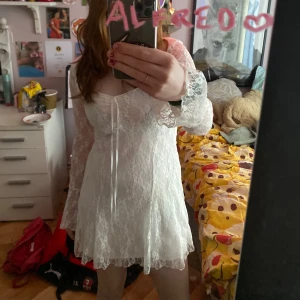 Vit spetsklänning - Säljer en romantisk vit spetsklänning med långa ärmar och v-ringad design. Klänningen har en kort längd och är perfekt för speciella tillfällen. Den har fina spetsdetaljer som ger en elegant touch. Har använt en gång på en skolavslutning, hör av er vid frågor!