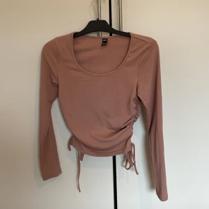 Rosa ribbad topp från Shein - Säljer en rosa ribbad topp från Shein med långa ärmar och knytning i sidan. Perfekt för en stilren look. Toppen har en rund halsringning och är i en mjuk och bekväm kvalitet.