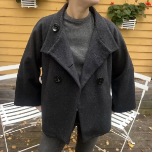 Mörkgrå kappa med trekvartsärm - Säljer denna mörkgrå kappa med stora knappar framtill och trekvartsärmar.
