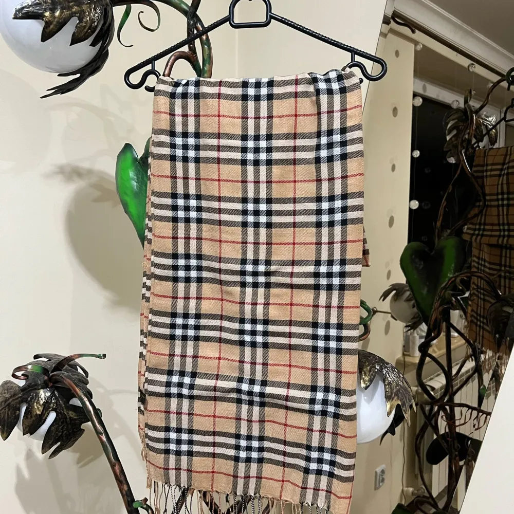 Snygg rutig halsduk i beige med svarta och röda ränder. Gjord av en blandning av pashmina och silke, vilket ger en mjuk och lyxig känsla. Perfekt för att hålla sig varm och stilren under kyliga dagar.Det ni ser på bilden är det ni får😁 ett plagg som är köpt i bulk så jag vet lila lite som ni, men jag har kollat så gott jag kan på alla möjliga sajter och det jag kan kolla stämmer överens med originalet väldigt bra tröja raka o fina sömmar, kvalitets tyg. Asusteet.