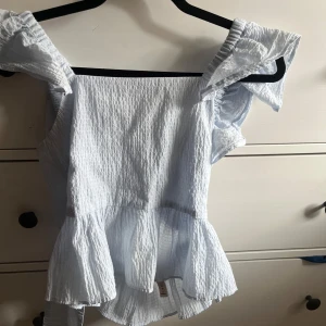 Ljusblå blus med volanger - Säljer en söt ljusblå blus med volanger och knytning i ryggen. Använd fåtal gånger och är i mycket bra skick!! Skriv om ni vill ha fler bilder💕