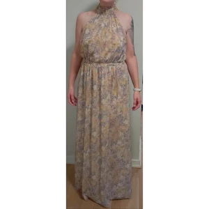 Blommig långklänning - Säljer en vacker blommig långklänning med mjuka pastellfärger. Klänningen har en elastisk midja och en halterneck-design som ger en elegant look. Perfekt för sommarens varma dagar. 🌸 Klänningen är aldrig använd då den var för lång för mig.