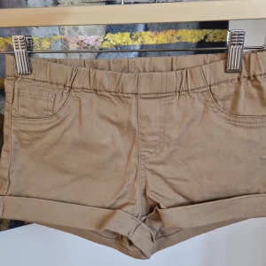 Beige shorts med fickor - Snygga beige shorts med elastisk midja och praktiska fickor bak. Perfekta för en avslappnad stil. De har en enkel design med uppvikta ben. Har fläck 