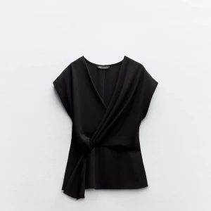 Svart omlottopp från Zara - Elegant svart omlottopp från Zara med en stilren design. Toppen har en v-ringad hals och knytning i sidan för en smickrande passform. Perfekt för en chic och modern look. Skicka prisförslag!💘