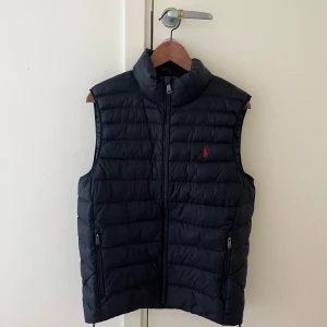 Ralph Lauren Väst - Snygg mörkblå dunväst från Ralph Lauren. Perfekt nu till våren och sommaren. Säljer då den aldrig kommer till användning. Använd max 5 gånger. Köpte den för ca 2100kr. Köpt från Zalando. Kvitto finns. Storleken är S men funkar även som M. Ser ut som ny. 
