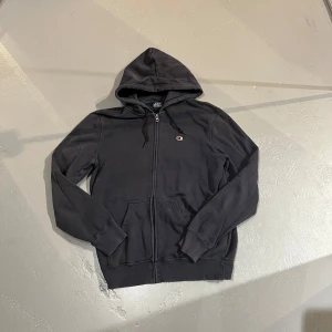 Mörkblå hoodie från Champion - Säljer en mörkblå hoodie från Champion i storlek medium. Den har en dragkedja framtill och en klassisk huva. Perfekt för en avslappnad stil.