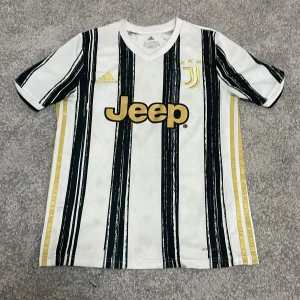 fotbollströja från Adidas - Snygg fotbollströja från Adidas med svart och guldiga detaljer. Tröjan har korta ärmar och ett randigt mönster. Perfekt för fotbollsfans som vill visa sitt stöd med stil.