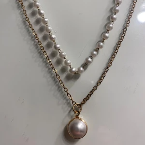 Halsband med pärlor och guldberlock - Elegant halsband med vita pärlor och en guldberlock med en stor pärla. Perfekt för att ge en klassisk touch till din outfit.