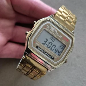 Guldfärgad digital klocka från Casio - Säljer en klassisk guldfärgad digital klocka från Casio med rektangulär display. Klockan har funktioner som alarm, kronograf och är vattentålig. Armbandet är i metall med justerbar spänne. Perfekt för dig som gillar retrostil! ⌚