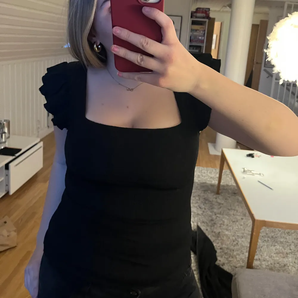 Snygg svart topp med volangärmar och fyrkantig urringning. Perfekt för en stilren look. Passar bra till både jeans och kjol.. Yläosat.