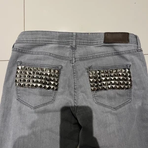 Grå jeans med nitar - Snygga grå jeans med coola nitar på bakfickorna. De har en unik design med slitna detaljer längs benen. 