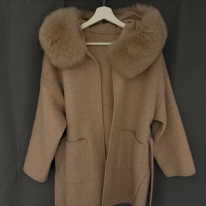 Beige kappa med pälskrage - Elegant beige kappa med stor huva och lyxiga pälsdetaljer. Äkta räv päls, kappan är i ull och kaschmir. Storlek XS, Oversized. Nypris 3299 kr