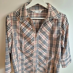 Rutig skjorta från Saint Laurent - Snygg rutig skjorta från Sara Louise i beige, svart och röd. Skjortan har trekvartsärmar och klassisk krage. Perfekt för en stilren look.