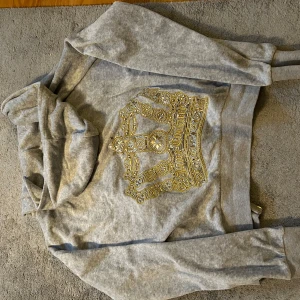 Grå hoodie från Juicy Couture - Säljer en grå hoodie från Juicy Couture med en stor guldfärgad krona på ryggen. Tröjan har dragkedja framtill och en mysig huva. 🤍🩶kolla in min profil så har jag matchade byxor (också Juicy Couture)